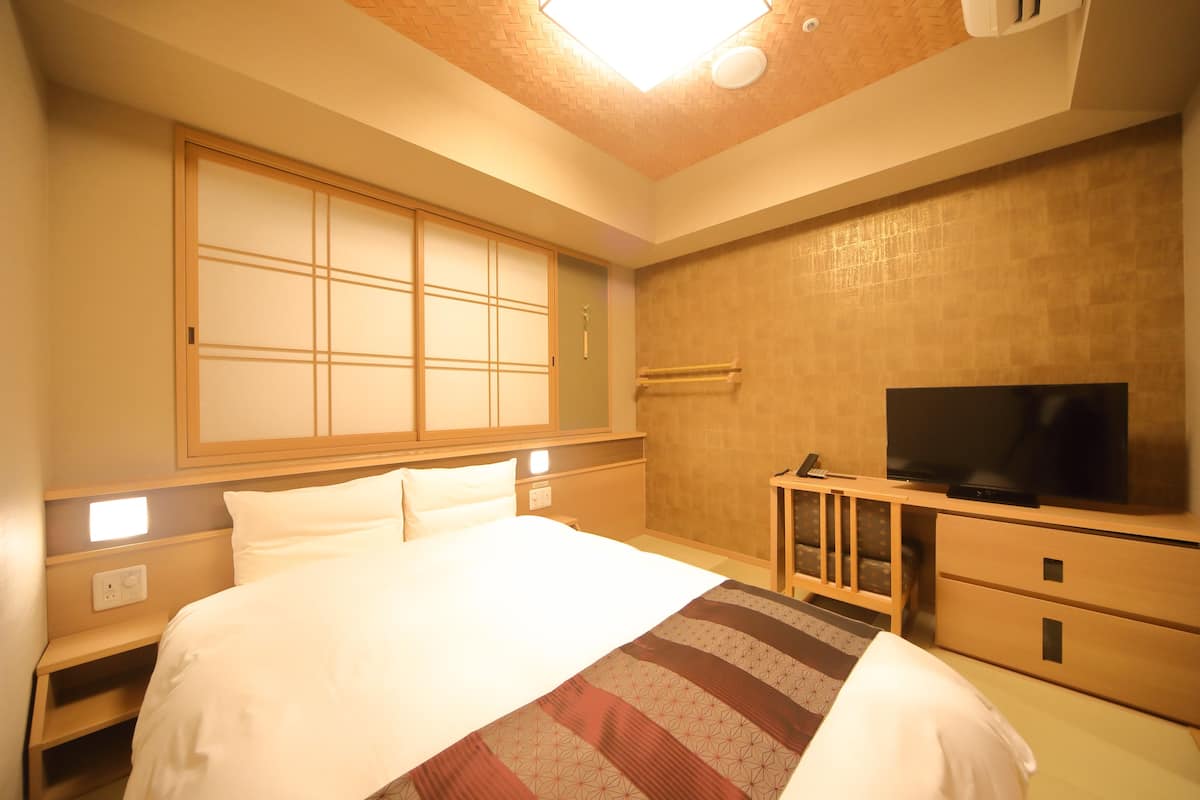 A hotel room with a large bed, a television, a wooden dresser, and a sliding shoji screen door.