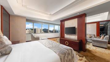 A hotel room with a large bed, a TV, a seating area, and a view of the cityscape.