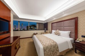 Habitación de hotel con una cama grande, televisión, escritorio y vista a la ciudad.