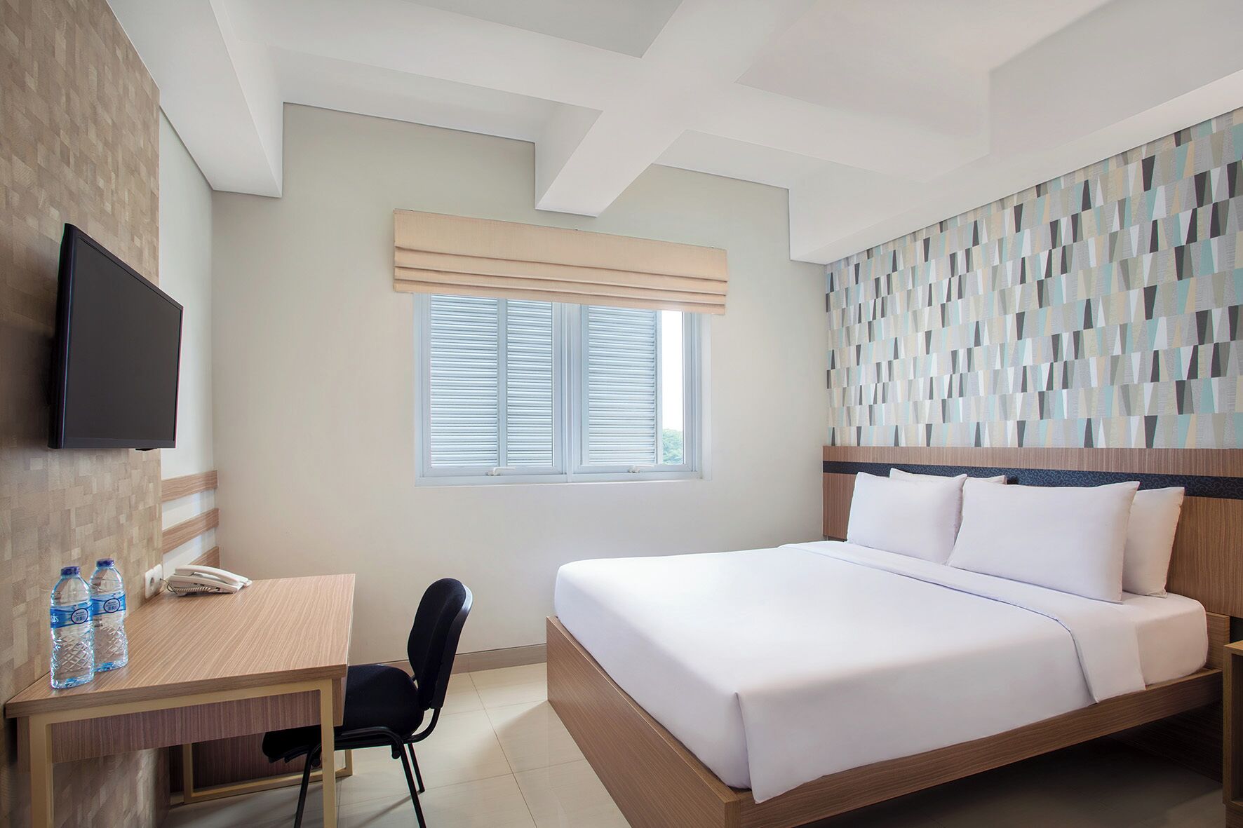 A hotel room with a bed, a desk with a chair, a television, and a window with blinds.