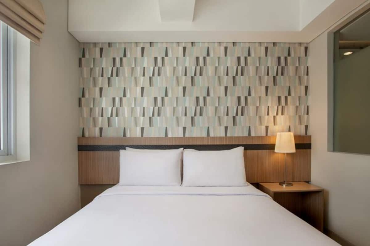 Ein Hotelzimmer mit Bett, Nachttisch, Lampe und einer Wand mit Muster.