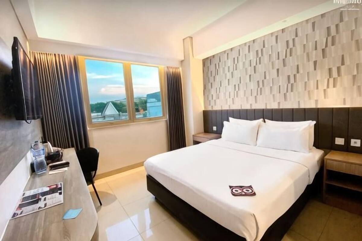 Ein Hotelzimmer mit Bett, Schreibtisch, Stuhl, Fernseher und einem fenster mit Vorhängen.