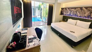 A hotel room with a bed, a desk with a menu, a TV displaying 'NETFLIX', and a view of an outdoor pool. - All Nite & Day Hotel - Alam Sutera (South Tangerang)