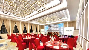 A conference room with red chairs and tables, a large screen displaying hotel information, and a patterned carpet. - All Nite & Day Hotel - Alam Sutera (South Tangerang)