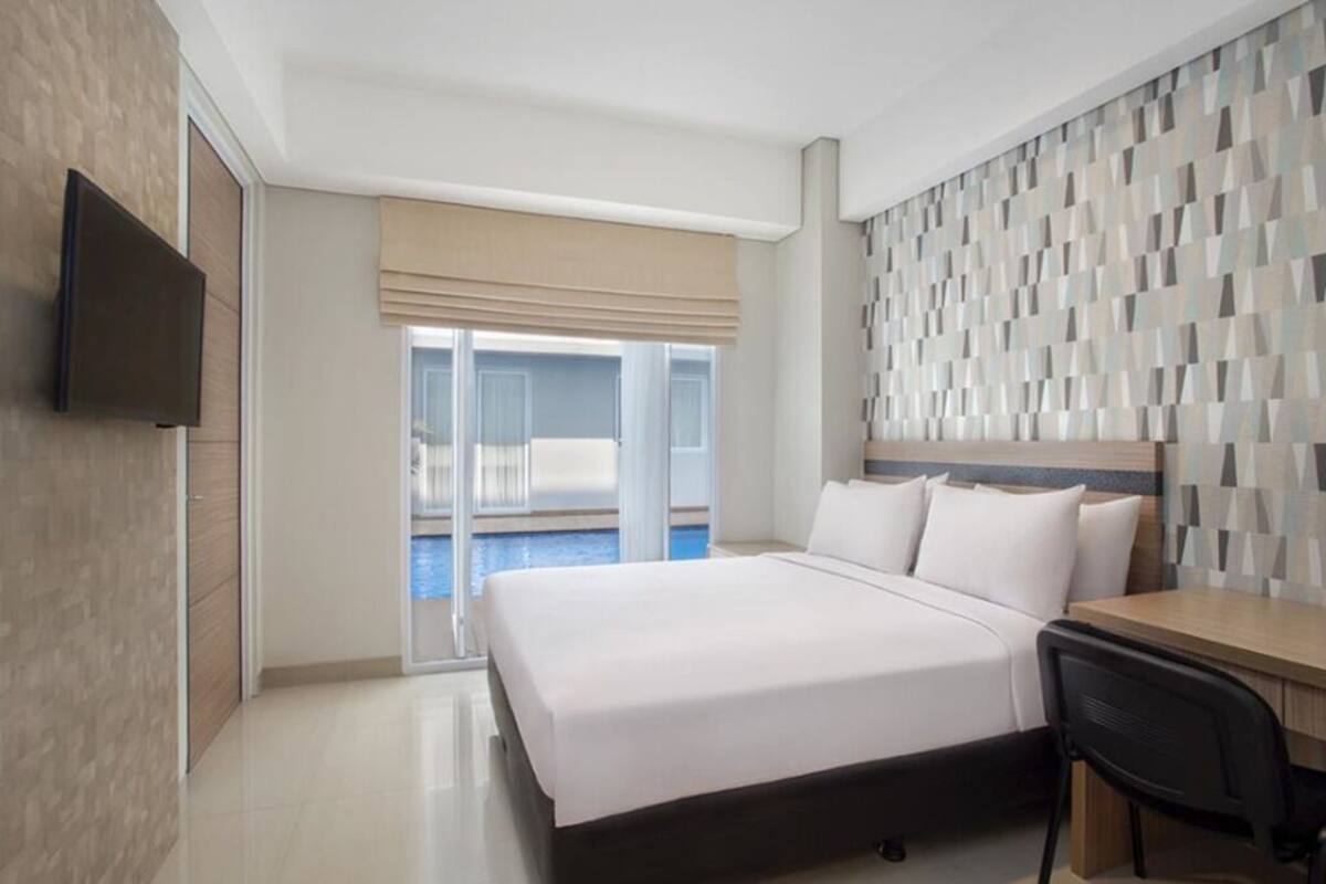 Ein Hotelzimmer mit Bett, Schreibtisch, Fernseher und Blick auf einen Pool.
