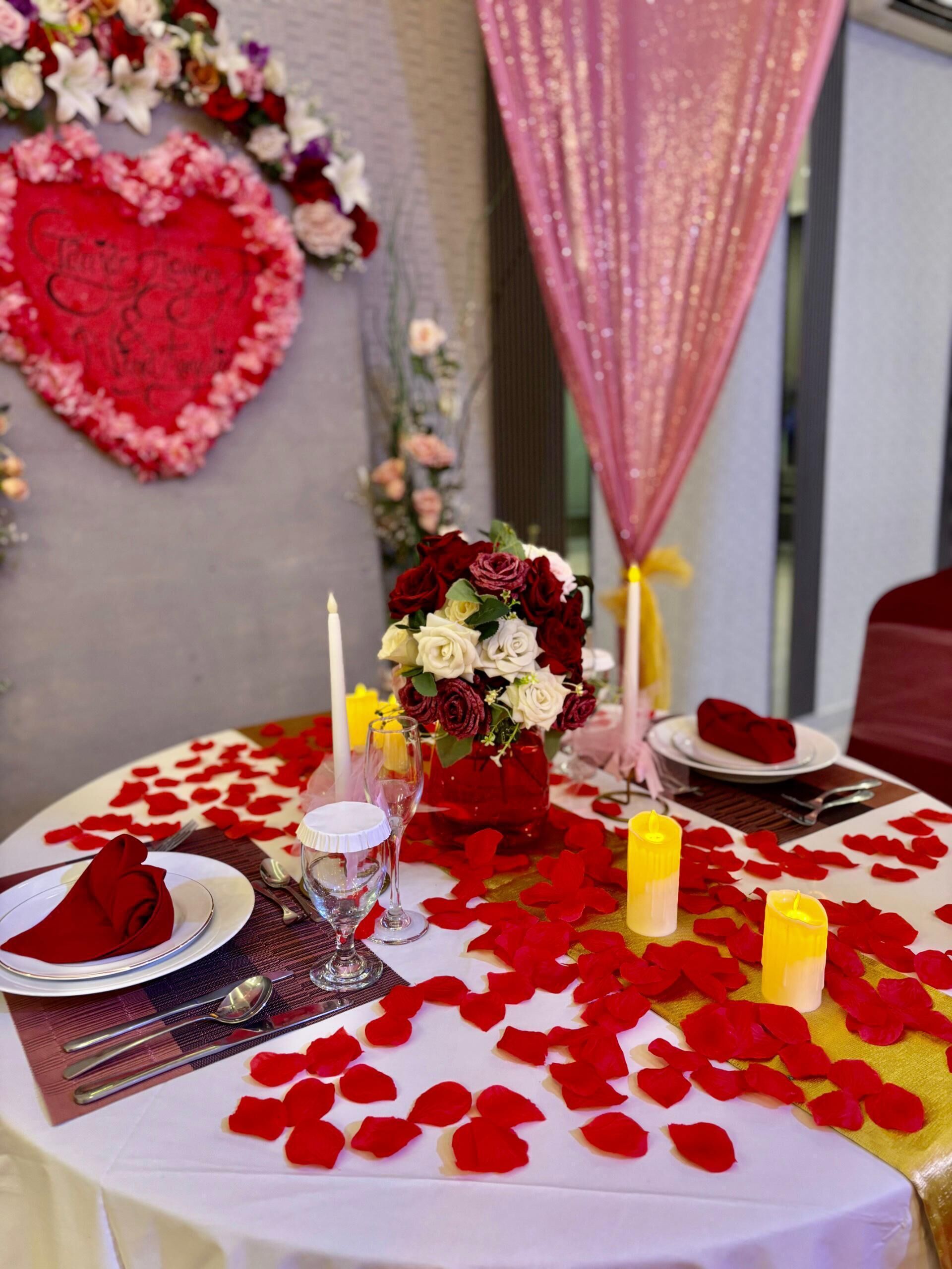 Een romantische diner setting met rozenblaadjes, kaarsen en een hartvormige decoratie.