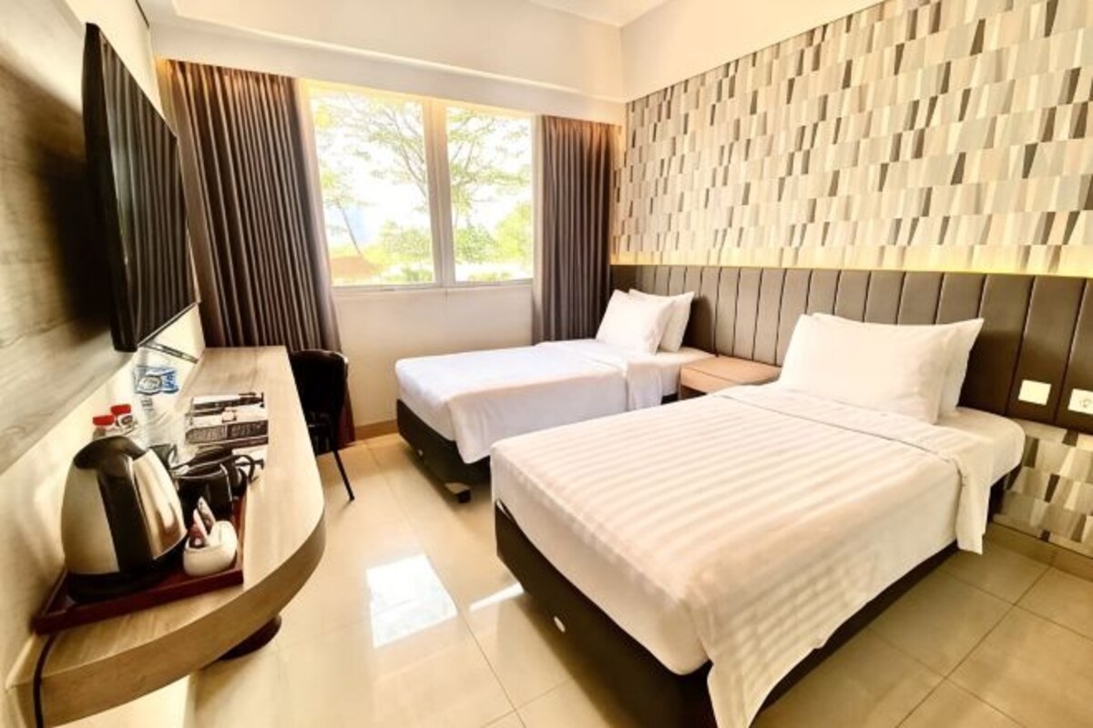 Habitación de hotel con dos camas, un escritorio con silla, televisión y ventana con cortinas.