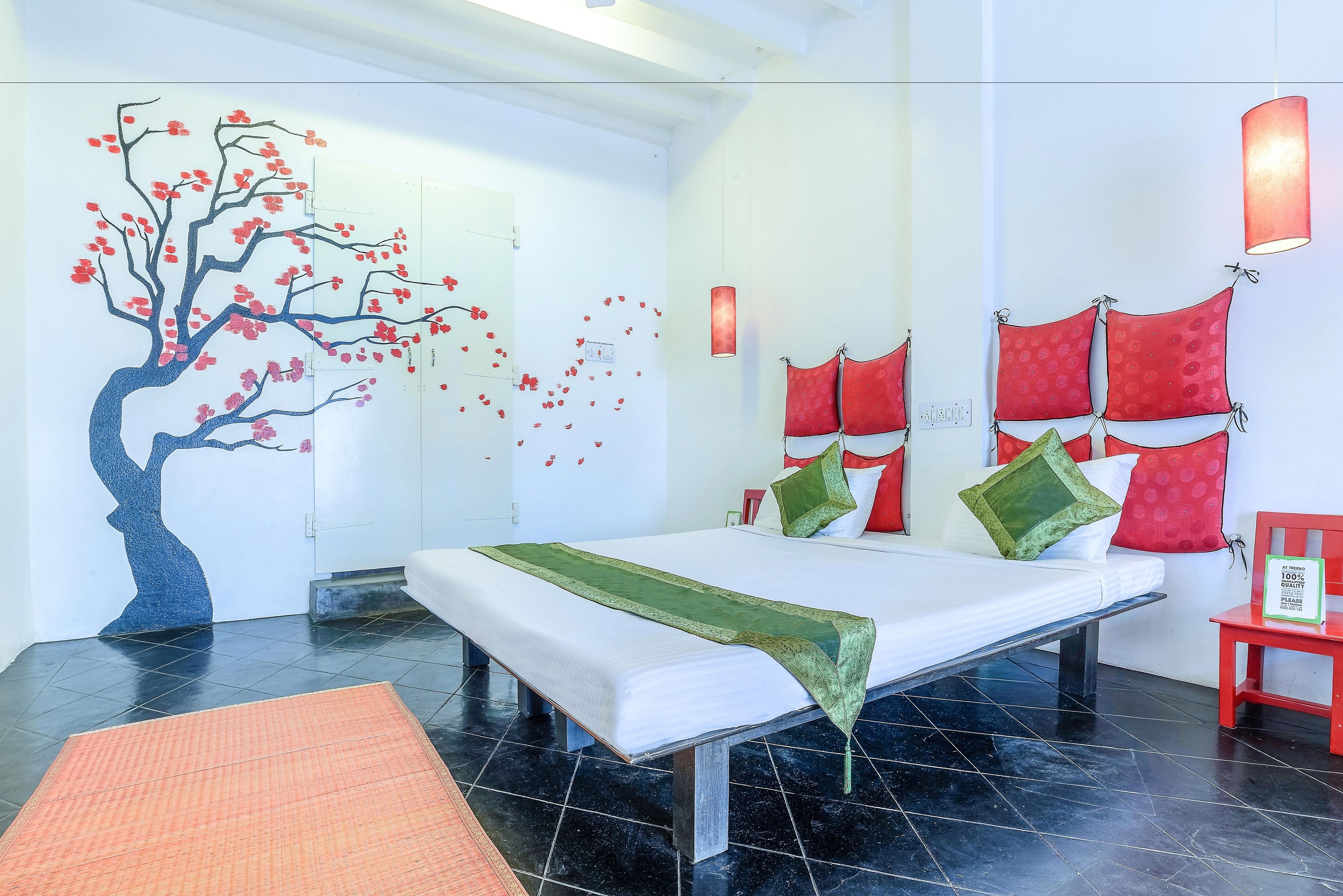 A modern hotel room with a large bed, a wall mural, and red decor accents.
