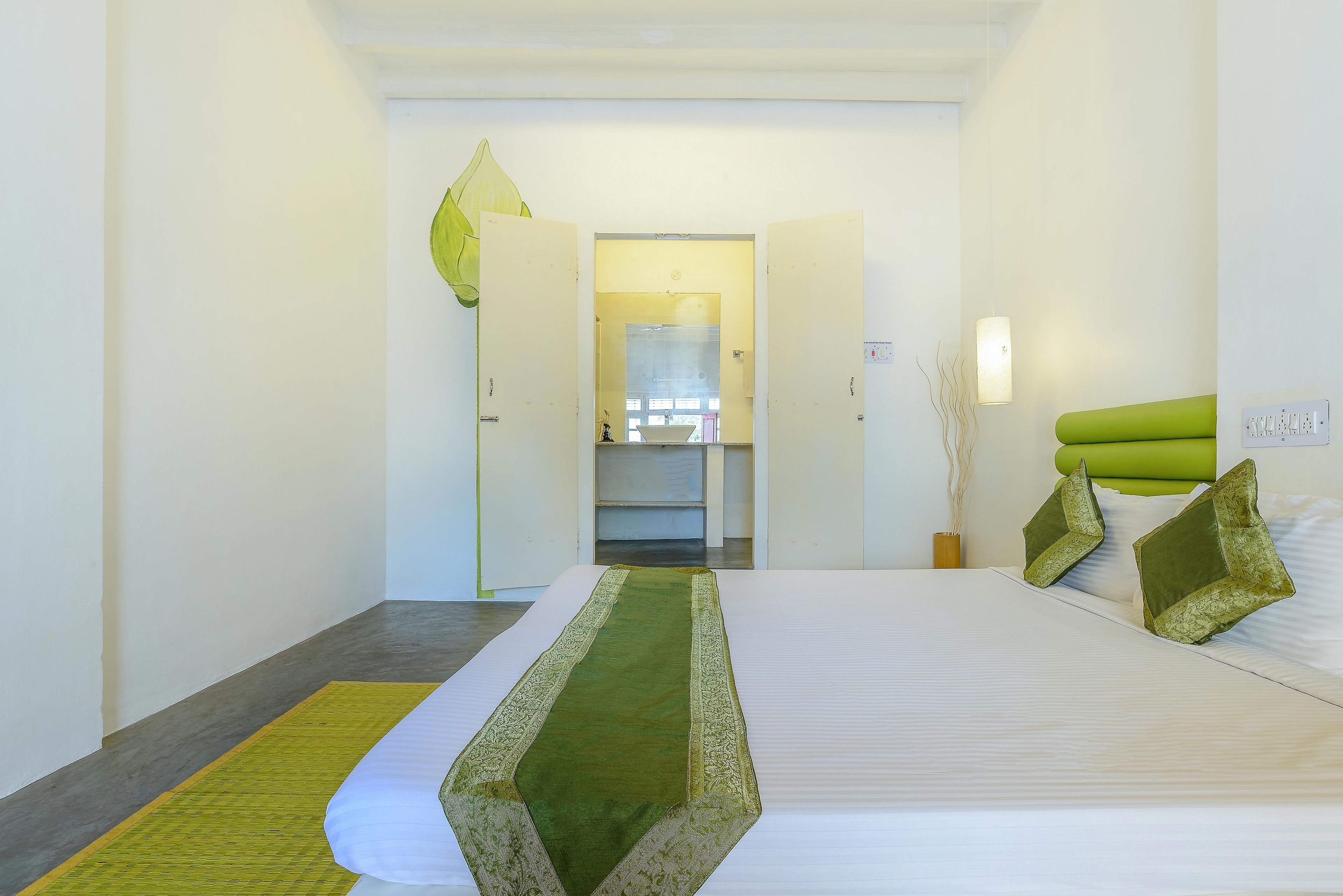 A hotel room with a large bed, a green runner, a green headboard, and a view into the bathroom.