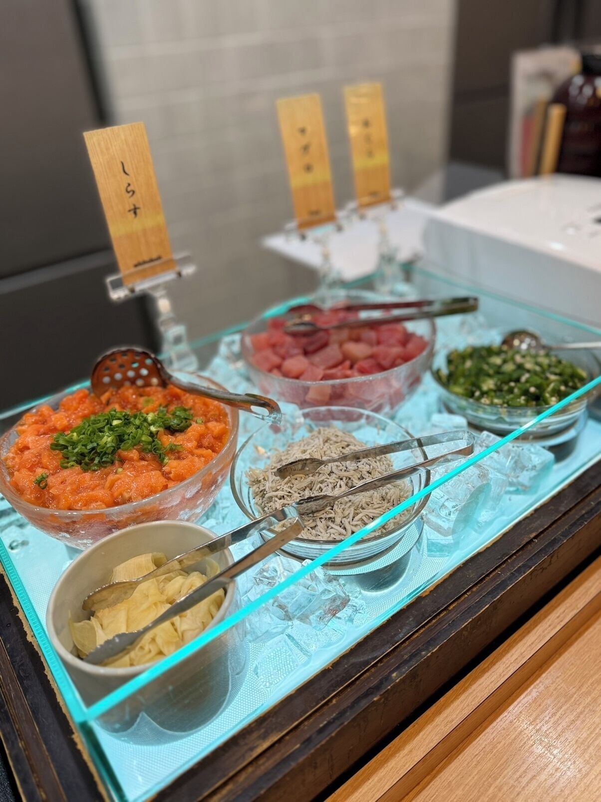 A buffet with various dishes, including a bowl of orange-colored food, a bowl of green vegetables, and a bowl of white food, all served on a glass tray with ice.
