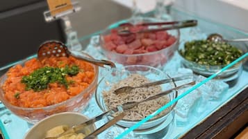 A buffet with various dishes, including a bowl of orange-colored food, a bowl of green vegetables, and a bowl of white food, all served on a glass tray with ice.