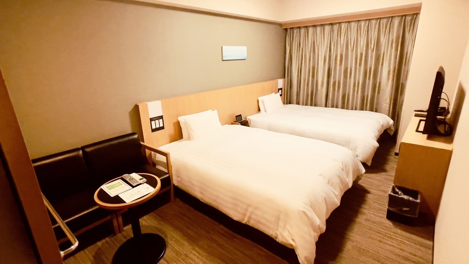 A hotel room with two beds, a desk with a chair, a television, and a window with curtains.