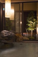 Un jardín interior tranquilo con fuente de agua, rocas y un árbol bonsái.