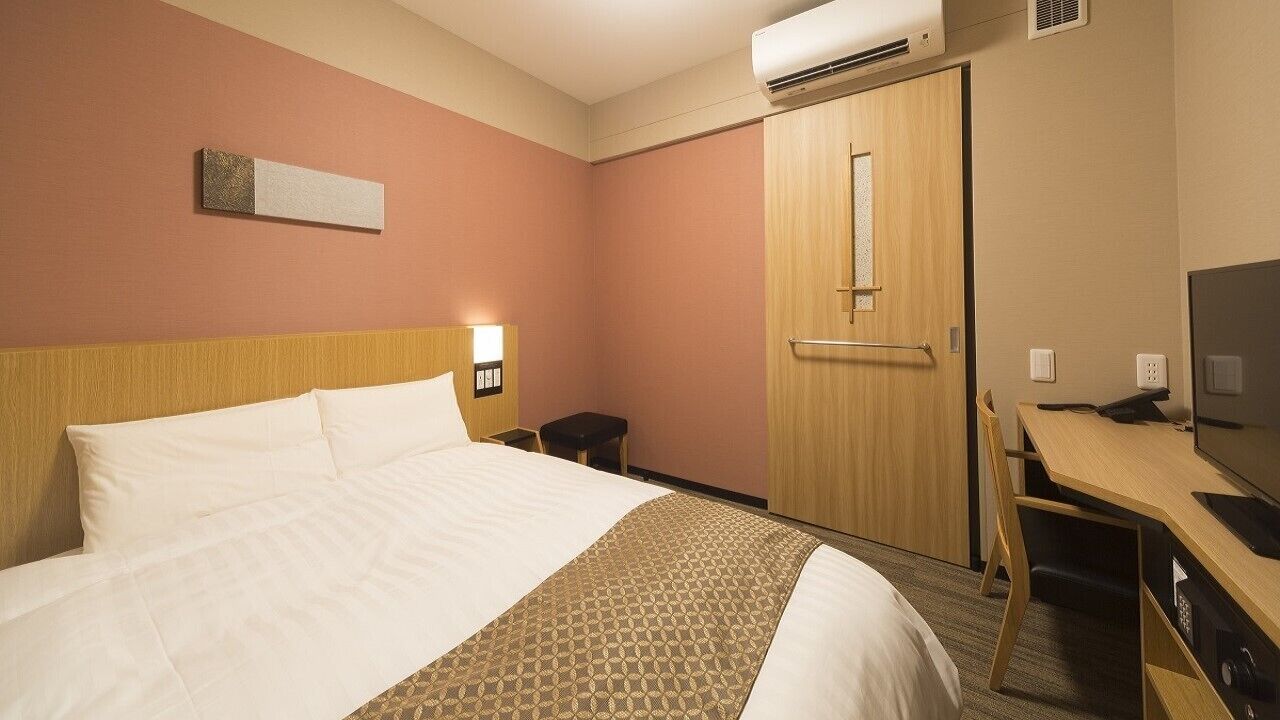 A hotel room with a bed, desk, chair, TV, and wardrobe.