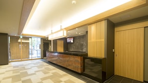 A modern hotel lobby with a check-in counter, a private room door, and a digital screen displaying information. - Dormy Inn Premium Tokyo Kodenmacho Hot Spring (Tokyo)