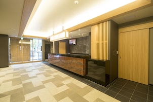 Un moderno vestíbulo de hotel con mostrador de recepción, puerta de habitación privada y una pantalla digital mostrando información.