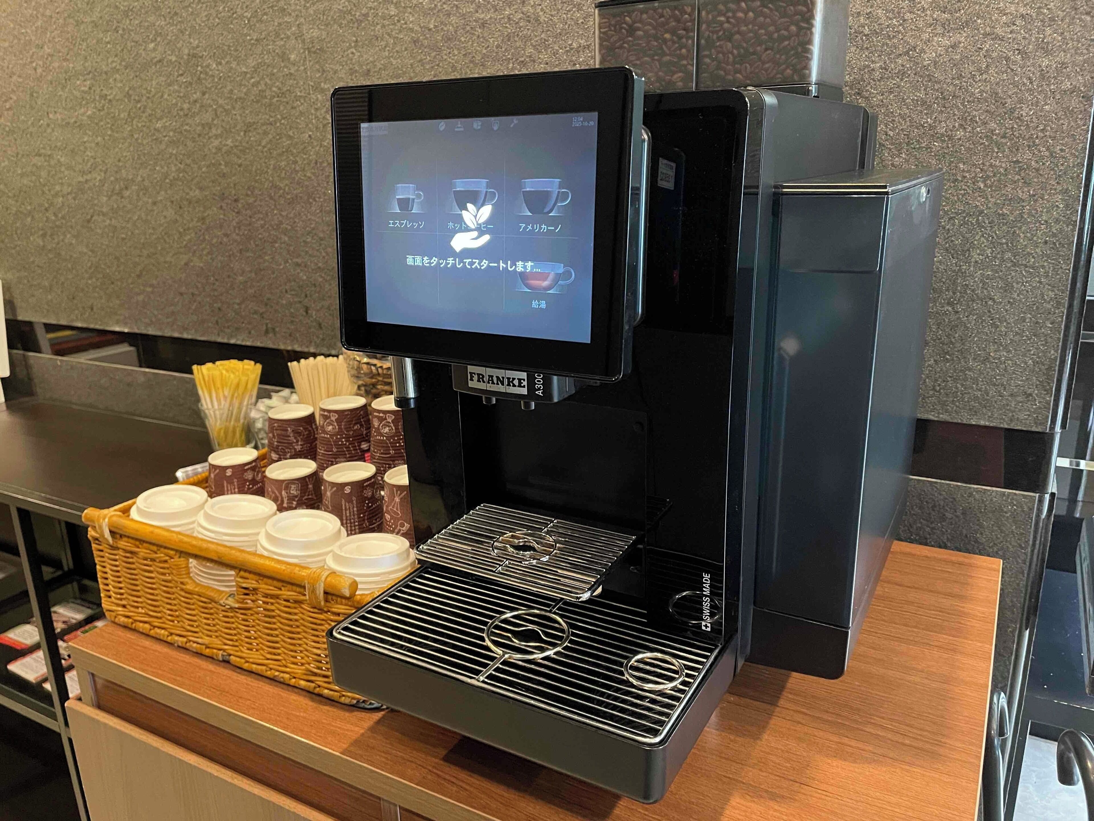 Una máquina de café con pantalla digital, un cesto de vasos desechables y un molinillo de café.