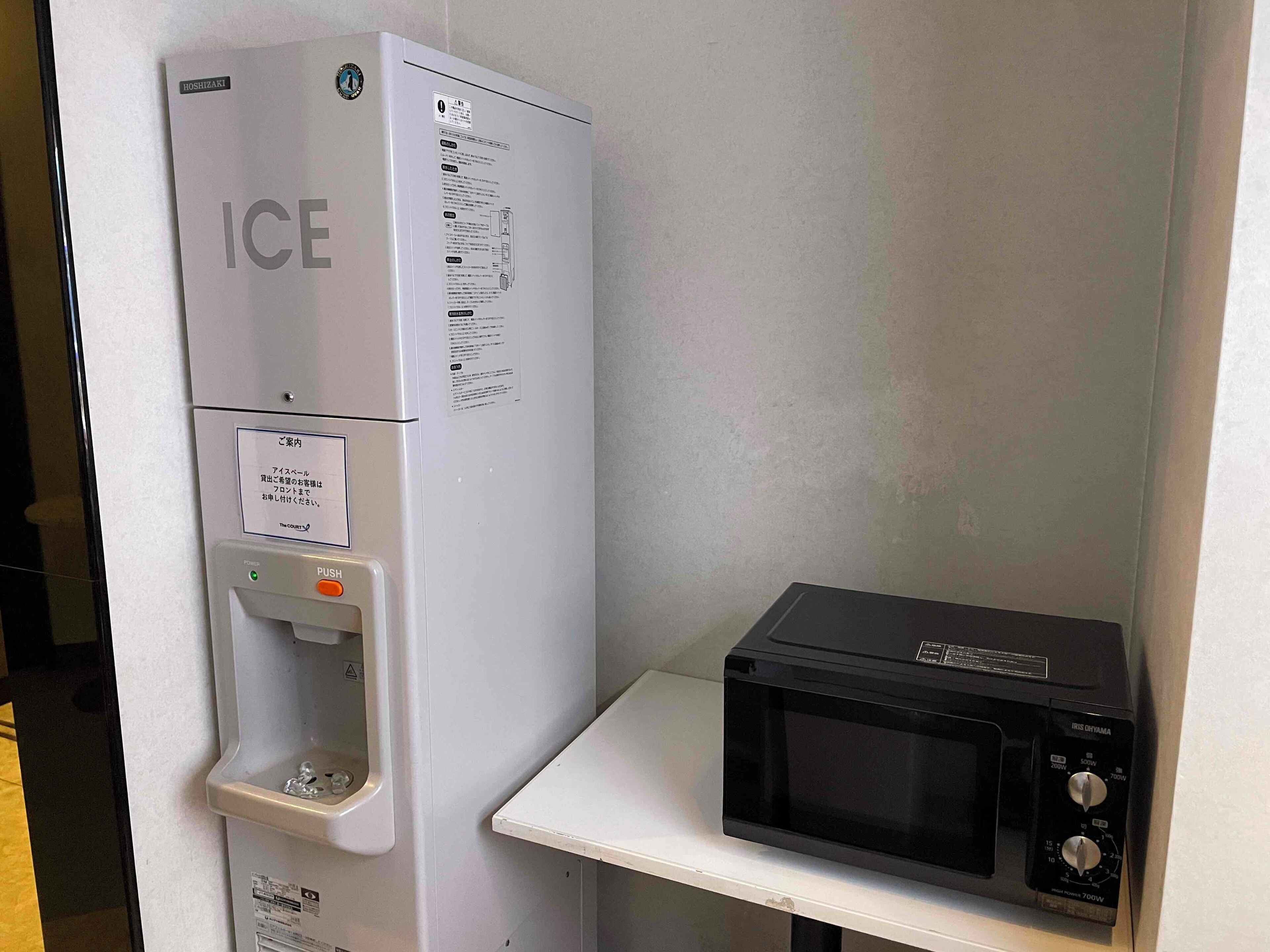 A compact kitchenette with a refrigerator labeled "ICE," a water dispenser, and a microwave on a white countertop.
