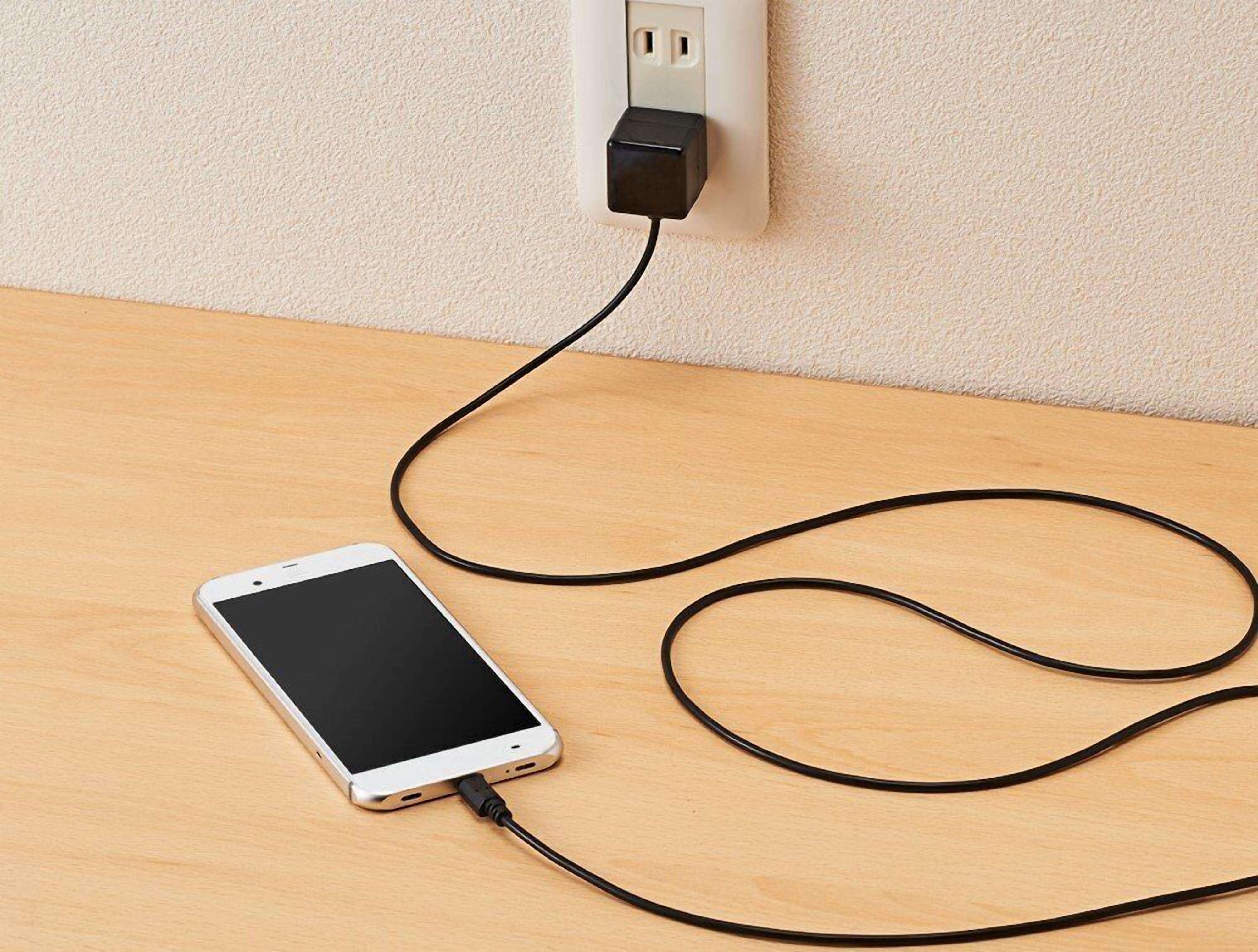 A smartphone connected to a wall socket on a wooden surface.