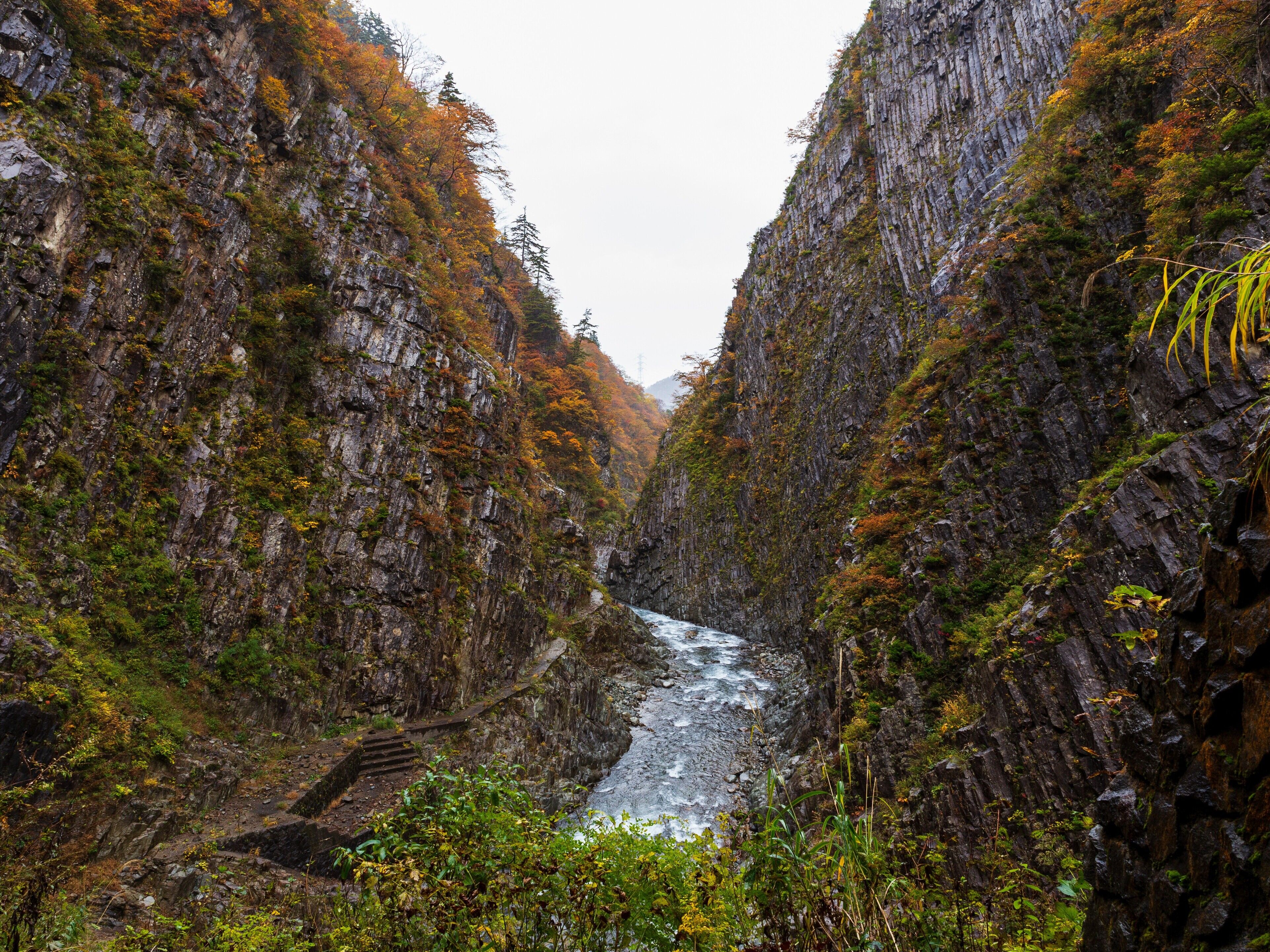 En smal kløft med en flod, omgivet af klippevægge og vegetation.