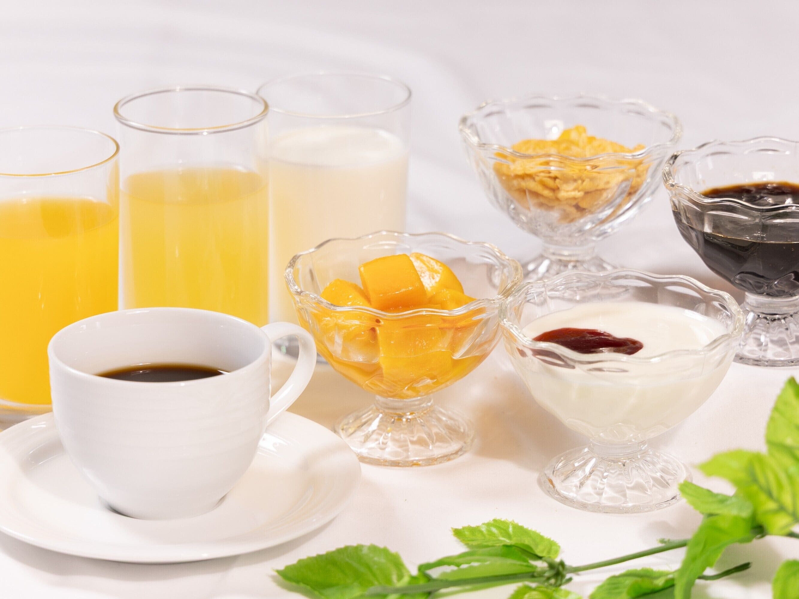A breakfast setting with a cup of coffee, a glass of orange juice, a glass of milk, a bowl of cereal, a bowl of yogurt with fruit, and a glass of dark liquid, likely coffee or tea.
