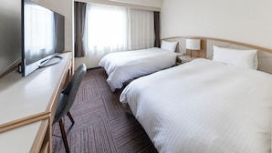 Habitación de hotel con dos camas, un escritorio con televisor, una silla y un ventanal con cortinas.