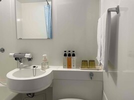 Um banheiro com pia branca, espelho, porta-toalhas e artigos de higiene no balcão.
