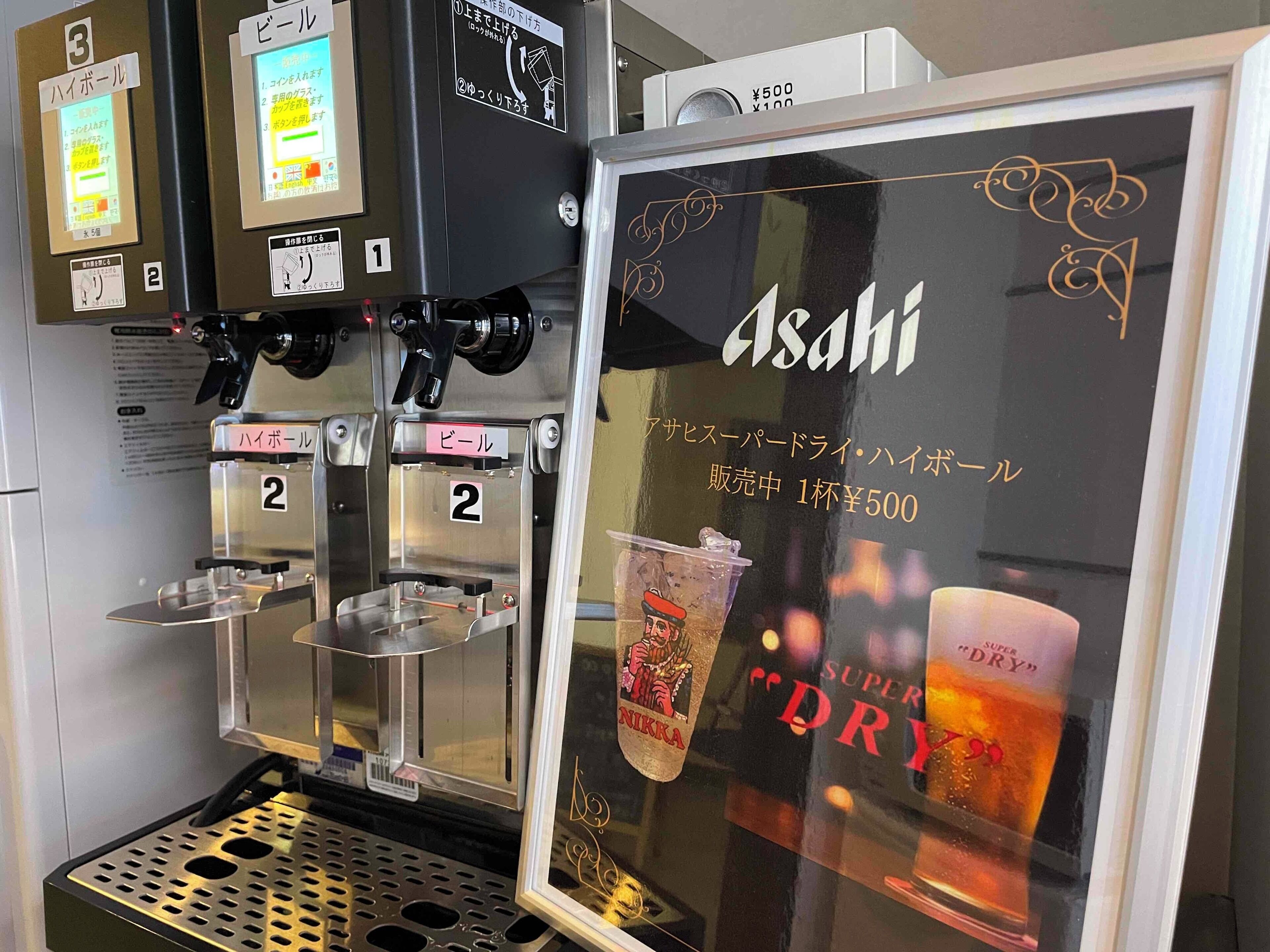 Máquina expendedora de bebidas con vitrina de vidrio que anuncia Asahi Super Dry.
