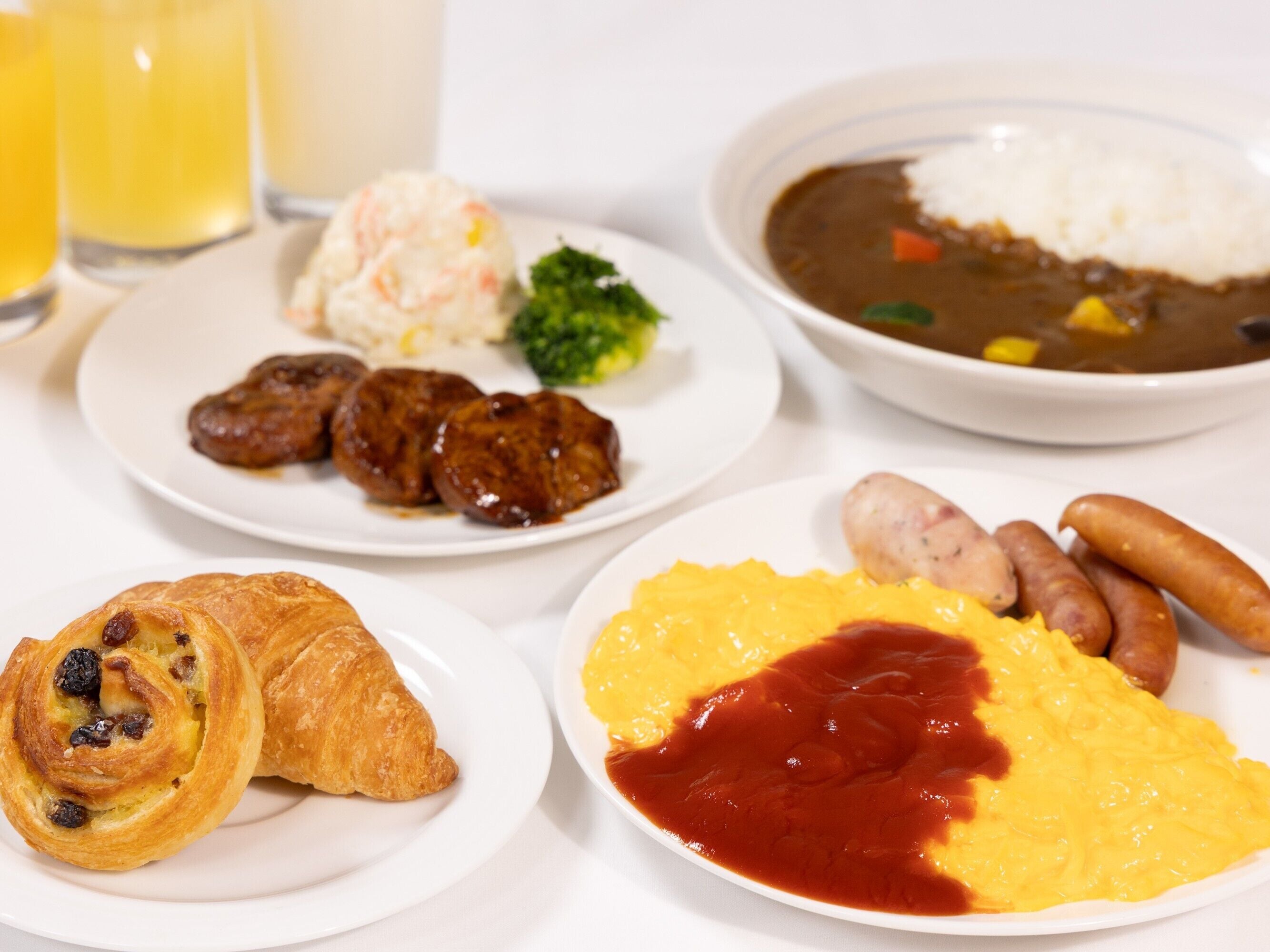 Un plato de desayuno con huevos, salchichas, cruasanes y un bol de sopa.