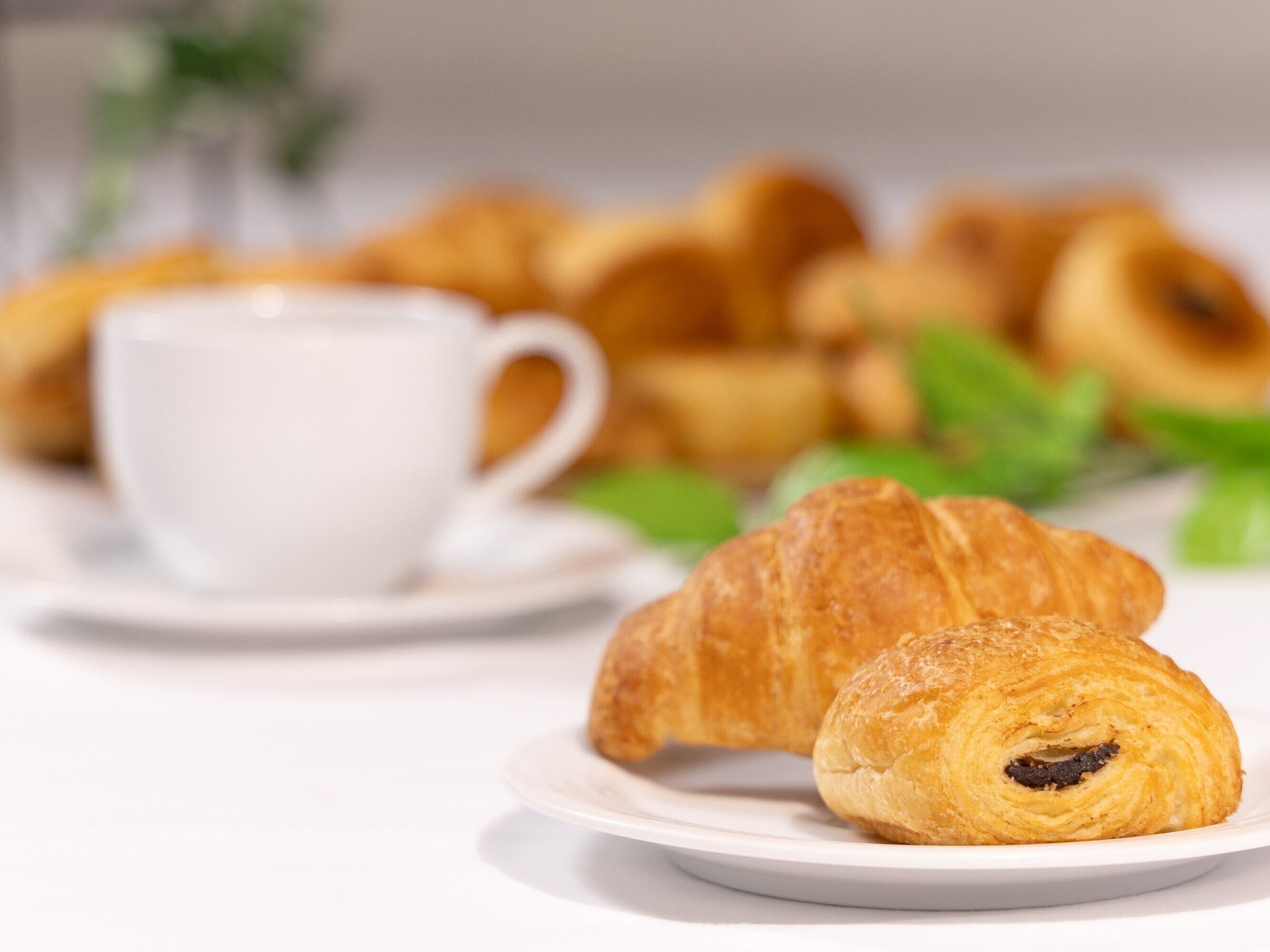 Une assiette avec un croissant et une tasse de café sur une table blanche.