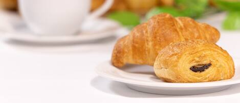 Une assiette avec un croissant et une tasse de café sur une table blanche.