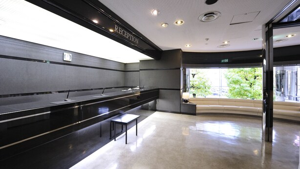 Un área de recepción moderna con un mostrador, un banco y una puerta de cristal que da al exterior.