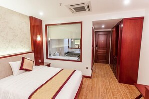 Hotellihuone, jossa on suuri sänky, peili, vaatekaappi ja pieni kylpyhuone, joka näkyy ikkunasta.