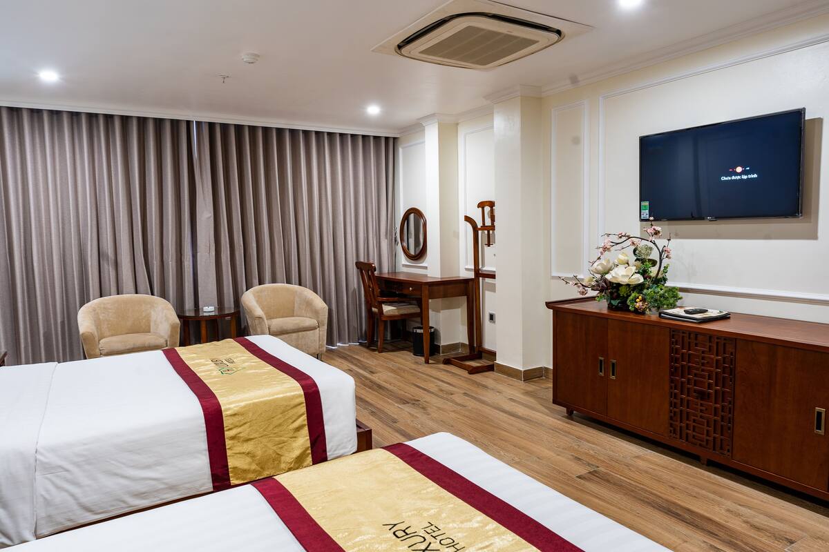 Ein Hotelzimmer mit zwei Betten, einem Fernseher, einer Holzkommode und einem Essbereich mit Tisch und Stühlen.
