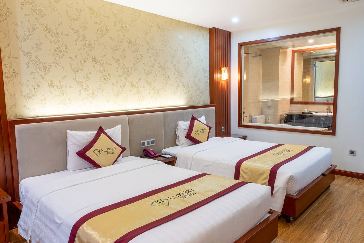 Ein Hotelzimmer mit zwei Betten, einem großen Spiegel und einem durch das Fenster einsehbaren Badezimmer.