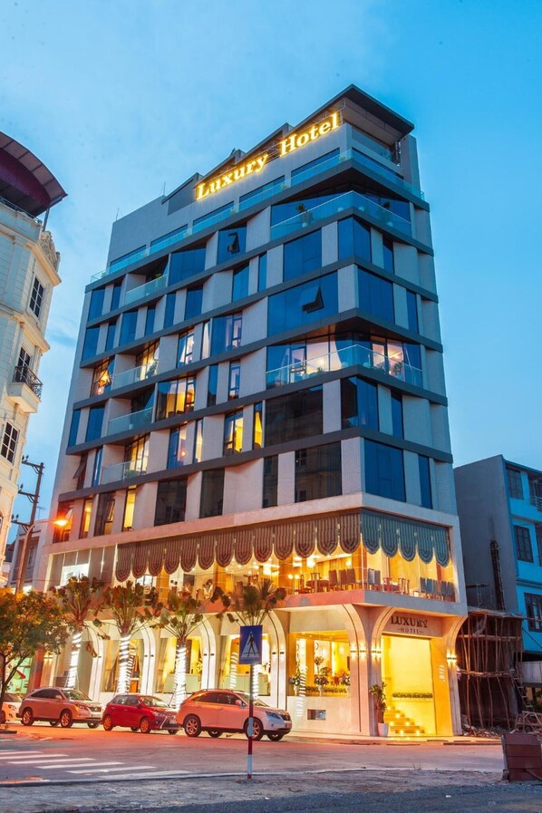 Un hotel de lujo de varios pisos con balcones, una entrada bien iluminada y un letrero visible.