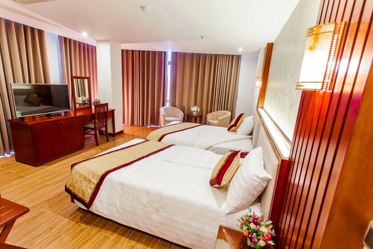 Ein Hotelzimmer mit zwei Betten, einem Fernseher, einem Schreibtisch und einem Sessel.
