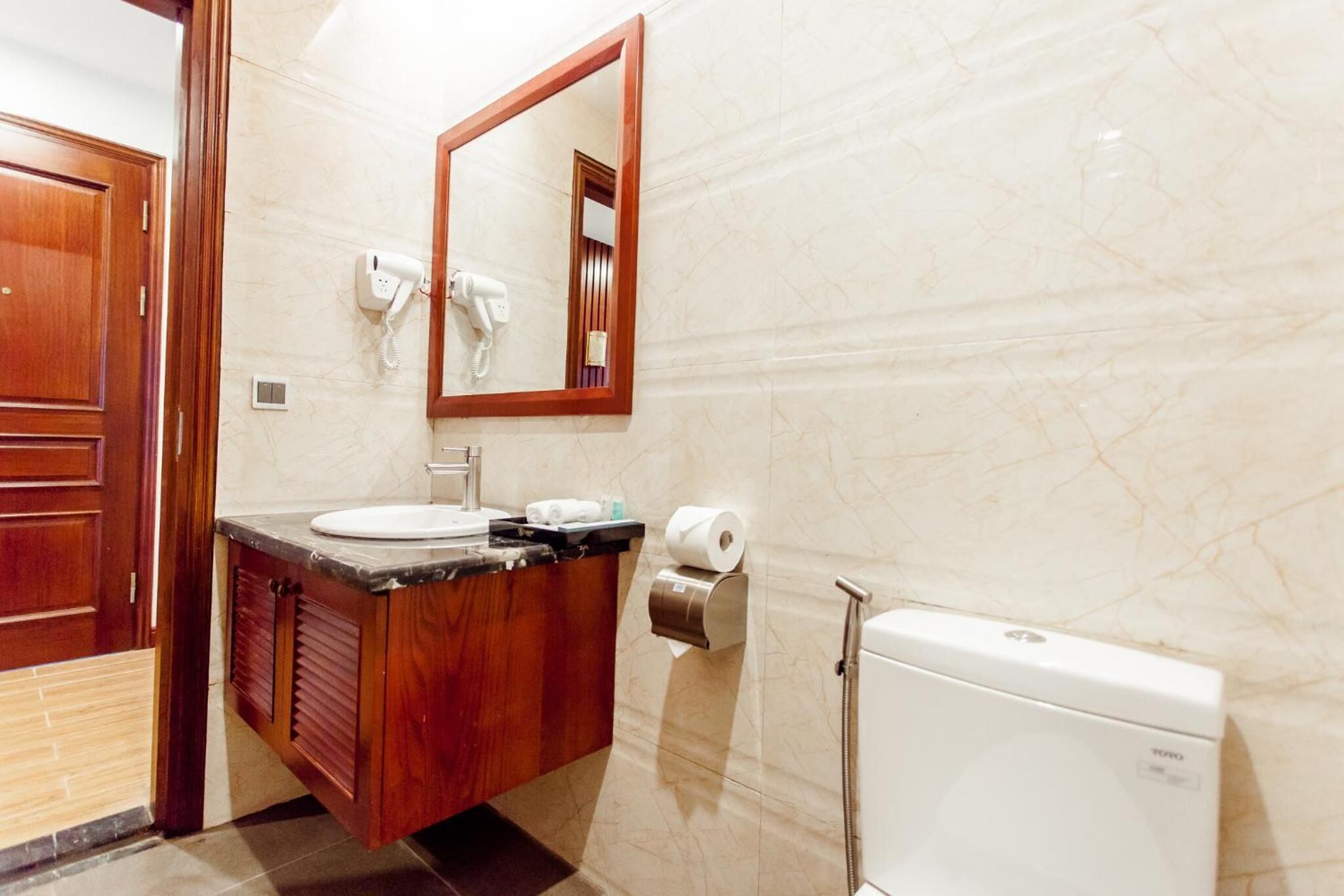 A bathroom with a wooden vanity, a mirror, a toilet, and a hand dryer.
