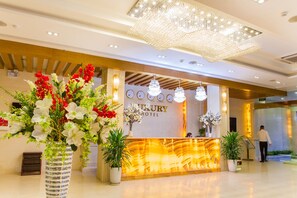 Zona de recepción de hotel con diseño moderno, que incluye un mostrador de recepción, candelabros y plantas en macetas.