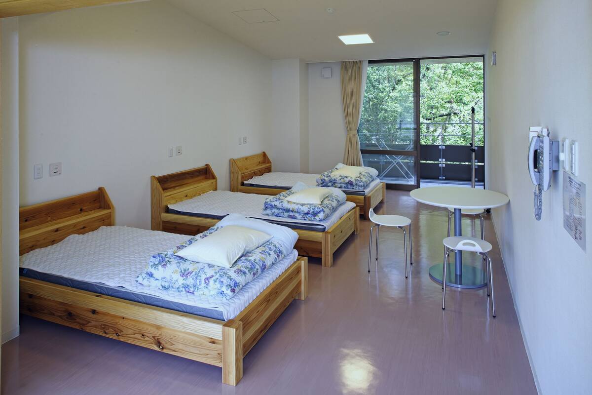Una habitación con tres camas de madera, una mesita redonda y un ventanal con vistas a zonas verdes.