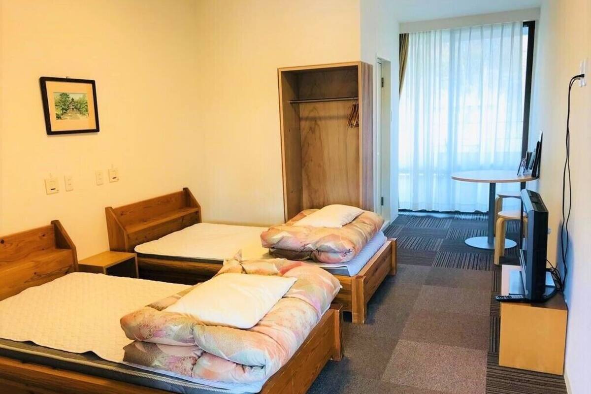 A hotel room with two wooden beds, a wardrobe, a television, and a small table.