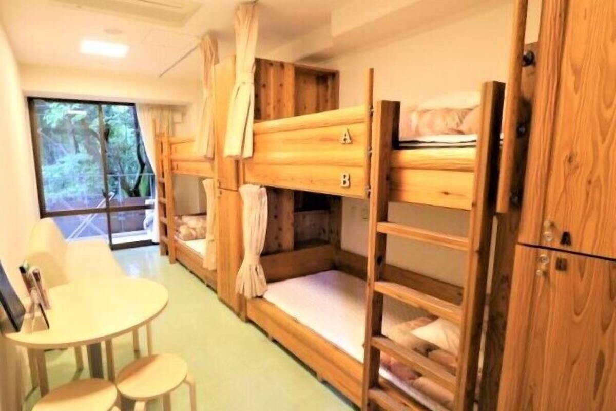 Un dormitorio con literas de madera, una pequeña mesa con sillas y vistas al exterior a través de una ventana.