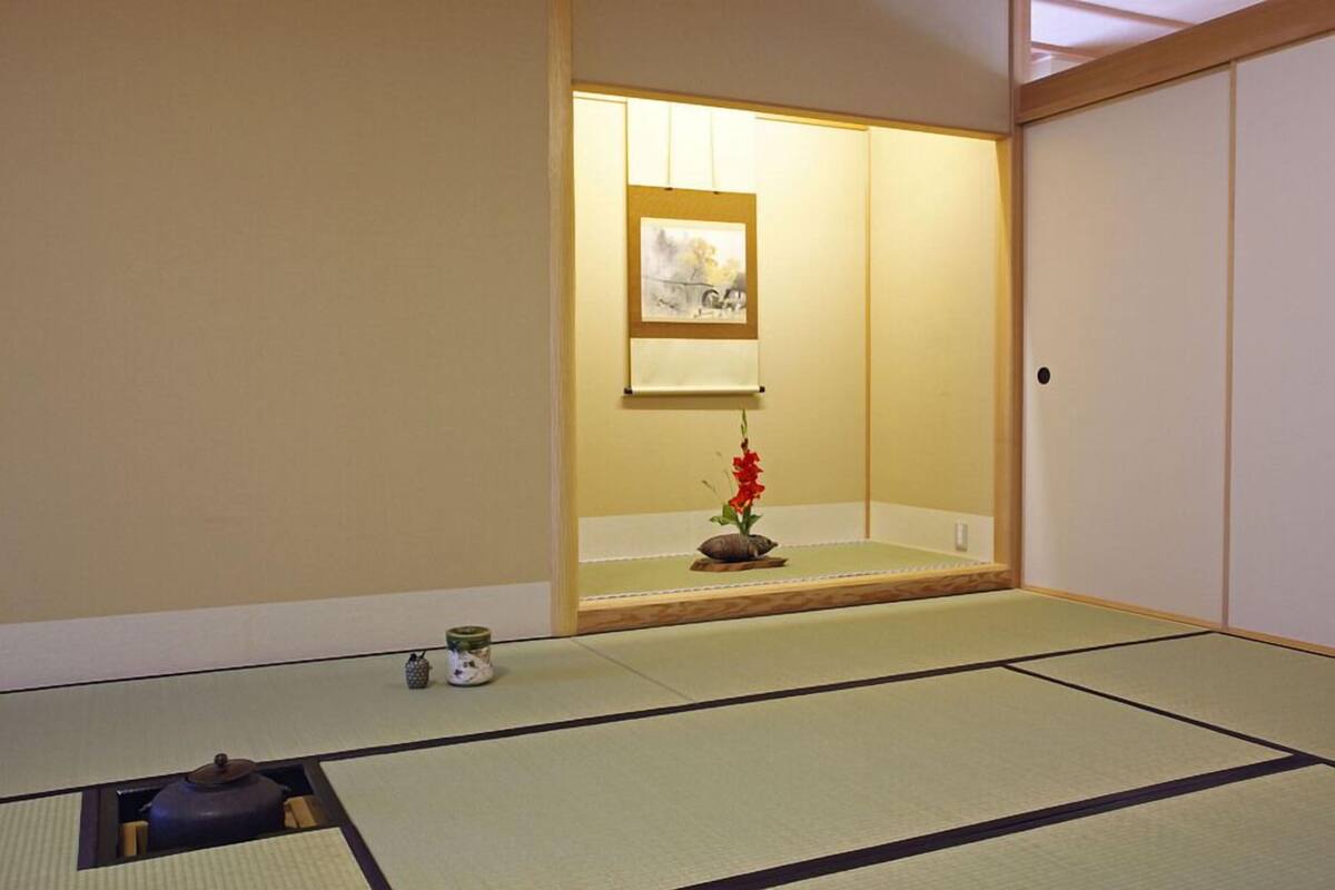 A tatami mat room with a shoji screen, a small table with a flower vase, and a picture frame on the wall.