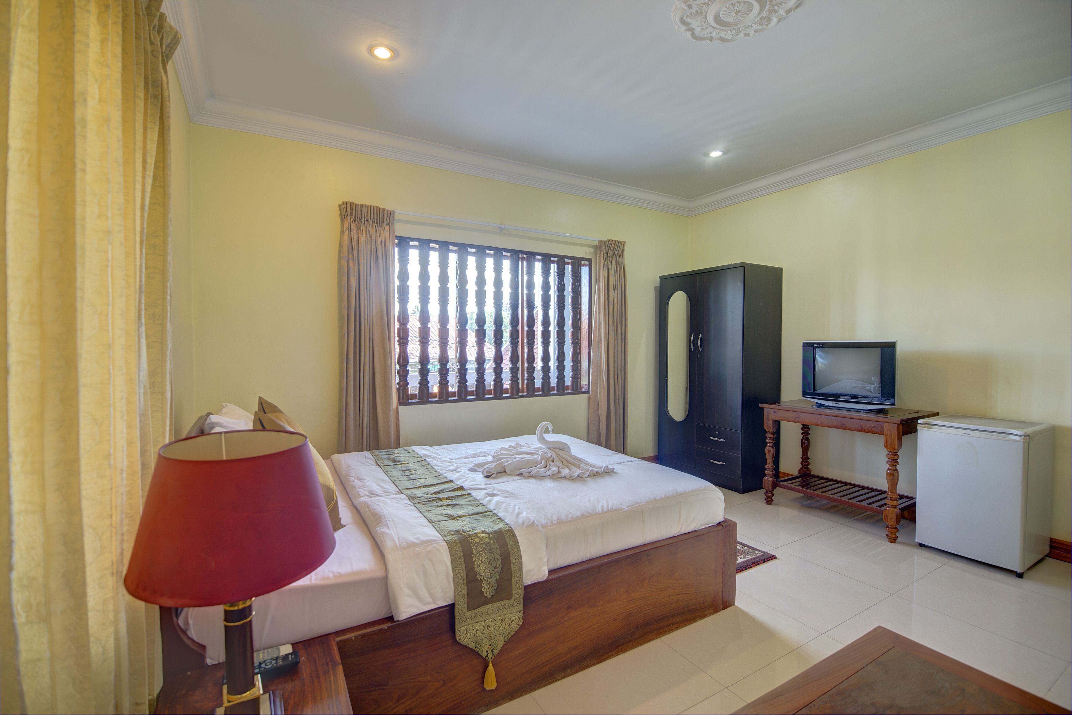 Una habitación de hotel con una cama, un televisor sobre una mesa de madera, un refrigerador pequeño y una ventana con cortinas.