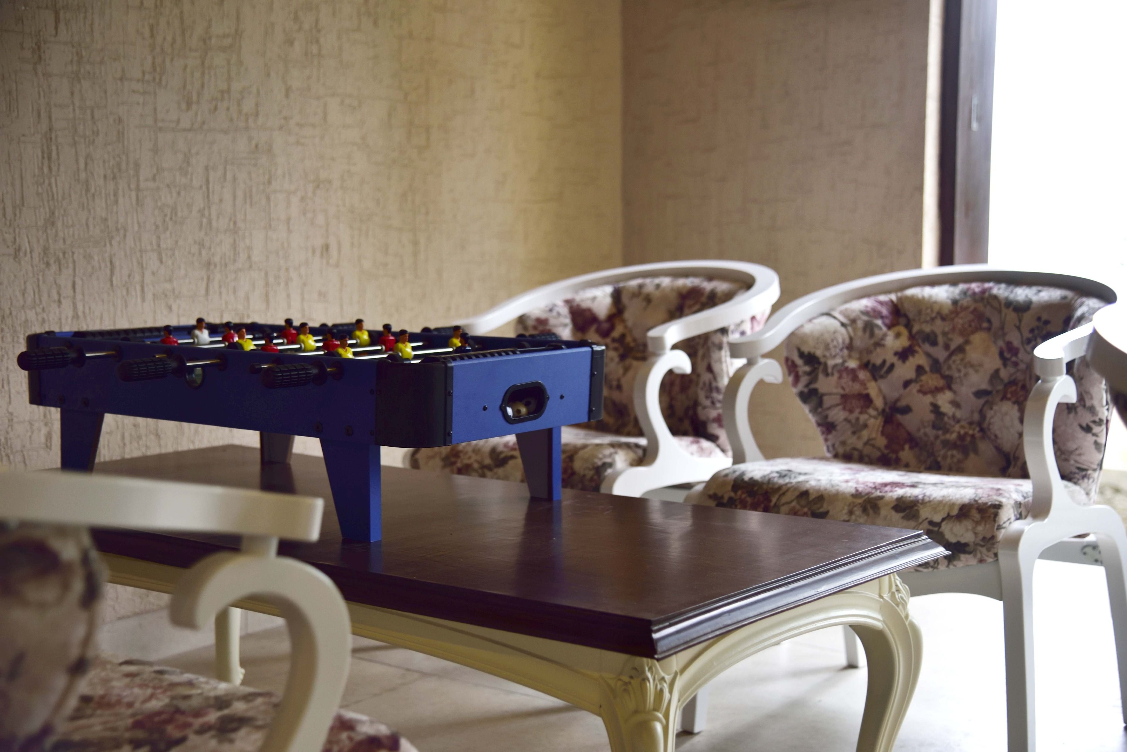 Une table de baby-foot dans une pièce où se trouvent des chaises à motifs floraux et une table en bois.