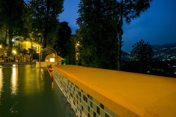 Una piscina con bordes de azulejos, rodeada de árboles y un edificio con ventanas iluminadas.