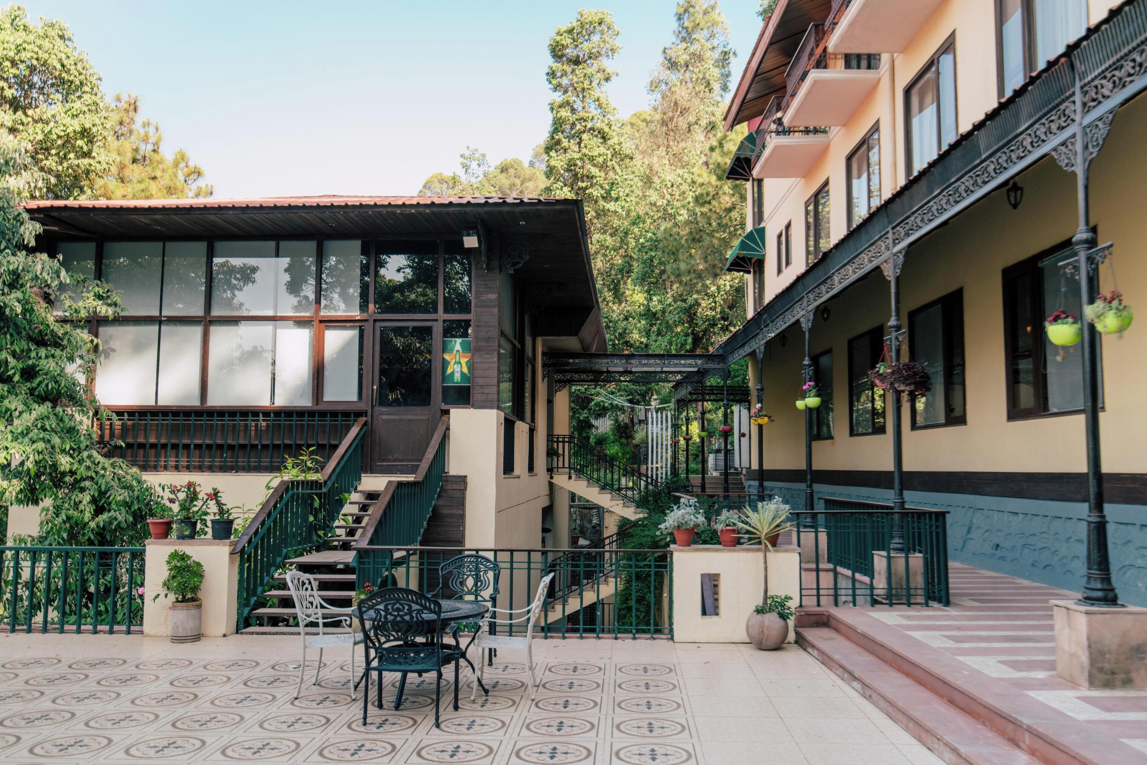 Un bâtiment doté d’un escalier menant à un balcon, lequel est entouré de plantes en pot et de mobilier d’extérieur.
