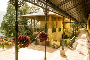 A covered outdoor area with a staircase leading to a yellow building, surrounded by potted plants and hanging flower baskets. - The Fern Hillside Resort Bhimtal (Nainital)