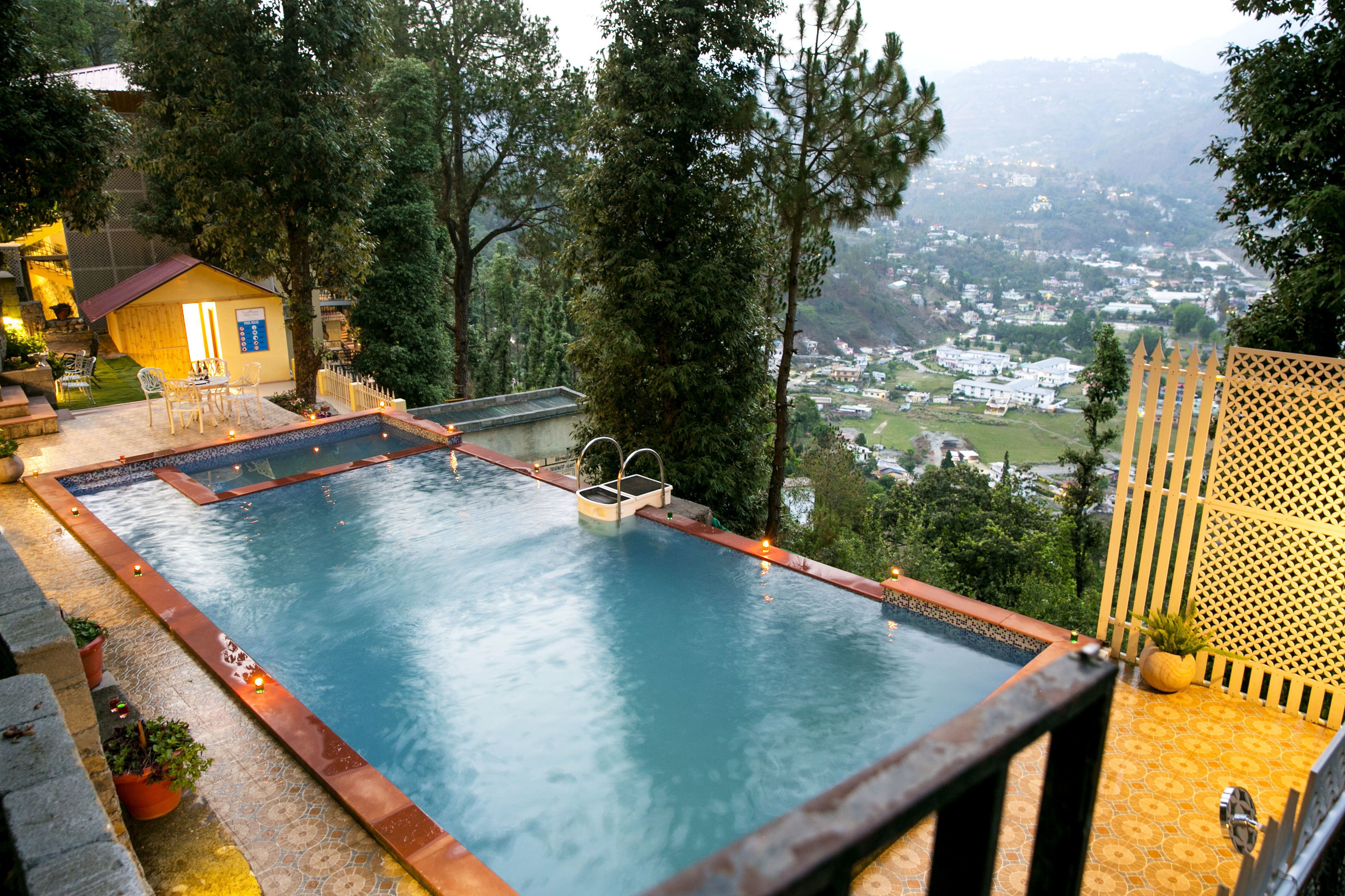 Une piscine rectangulaire avec une terrasse en bois et une petite maison en arrière-plan.