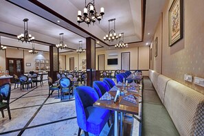 A hotel dining area with multiple tables, chairs, and a long bench along the wall. - The Fern Hillside Resort Bhimtal (Nainital)